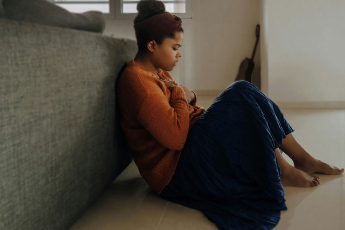 Person sitting on the floor, looking troubled, reflecting issues impacting mental health.