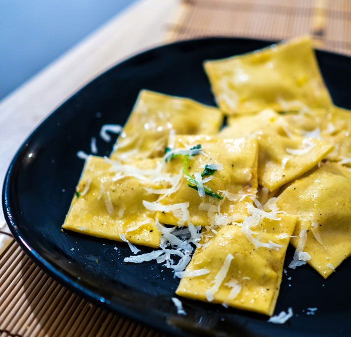 Lazy meal: Cheese ravioli on a black plate topped with grated cheese and herbs.