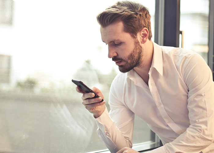 Man in white shirt looking at phone by a window, representing workplace red flags.