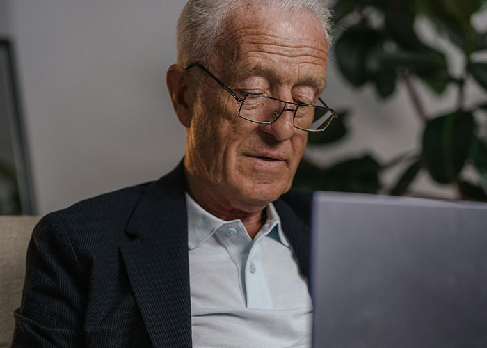 Elderly man using a laptop, reflecting on life without social media, wearing glasses and a suit jacket.