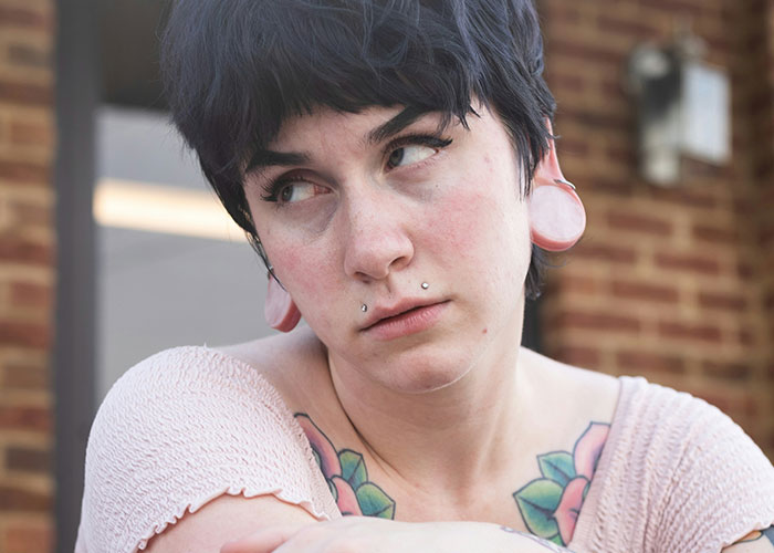 Person with a skeptical expression, piercings, and tattoos outdoors, symbolizing unserious reasons for brand boycotting.