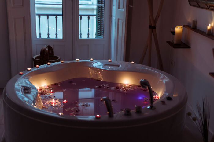 Round bathtub filled with purple water and floating candles in a dimly lit bathroom illustrating poorly-aging interior design trends.