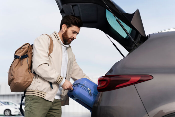 Man with backpack placing suitcase in car, illustrating work revenge theme.