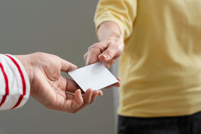 Two people exchanging a blank card, illustrating a subtle act of work-related revenge.