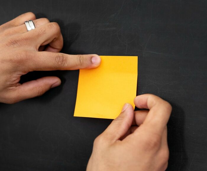Hands holding a sticky note, perfect setup for fun April Fools' pranks on a blackboard surface.