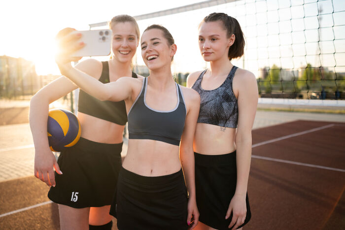 Three young women taking a selfie on a volleyball court, capturing a normal moment.