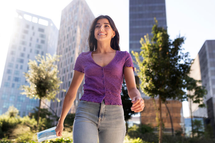 Woman in a purple top walks through an urban area, embracing “old people” habits with a cheerful expression.
