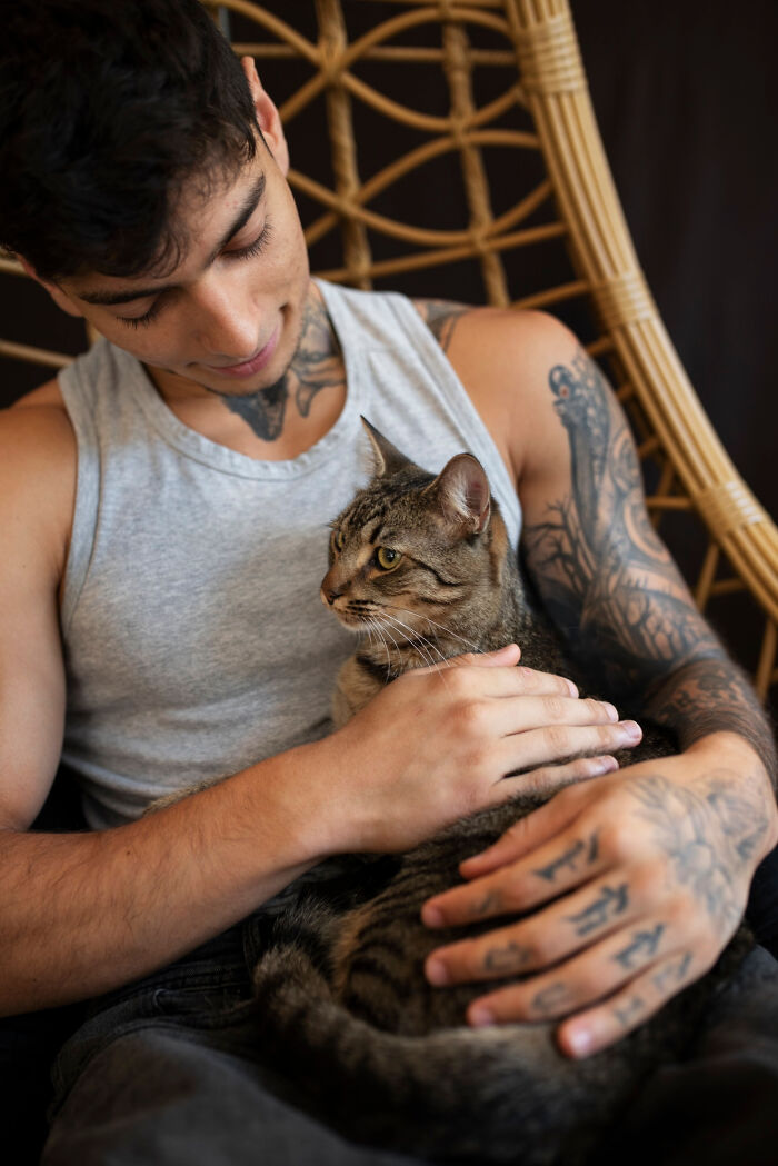 Man with tattoos in a gray tank top affectionately holding a cat, showcasing a green flag on a first date.
