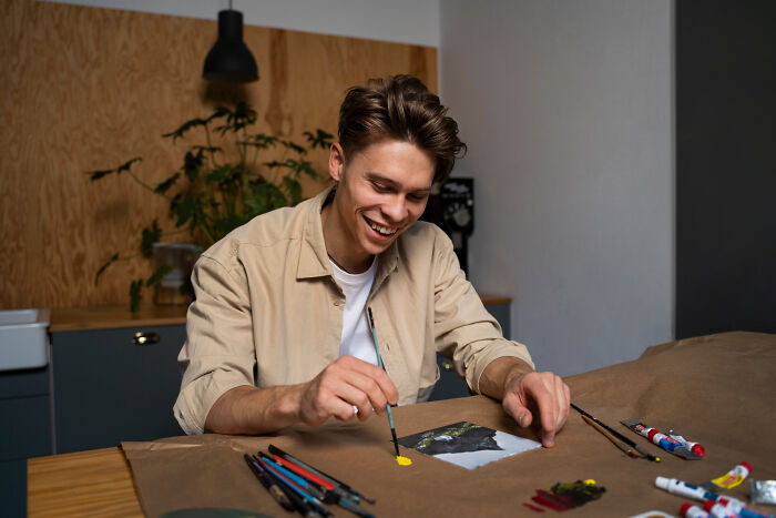 Man painting enthusiastically at a table, surrounded by art supplies, reflecting on what type to never date again.
