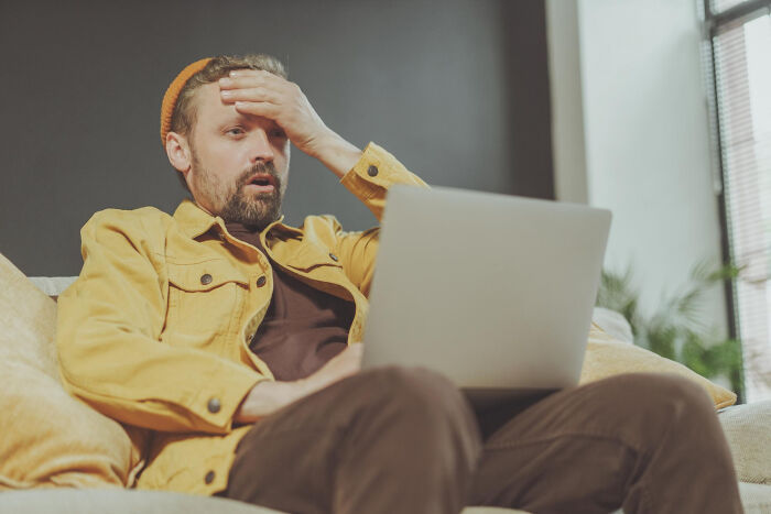 Man in a yellow jacket, looking surprised while using a laptop, possibly witnessing a savage act of revenge at work.