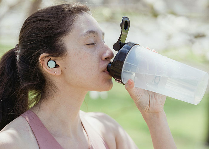 Young woman with earbuds drinking water, promoting beauty tips.