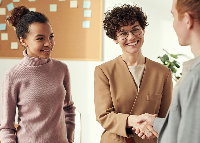 People smiling and shaking hands in an office, potentially masking toxic workplace red flags.