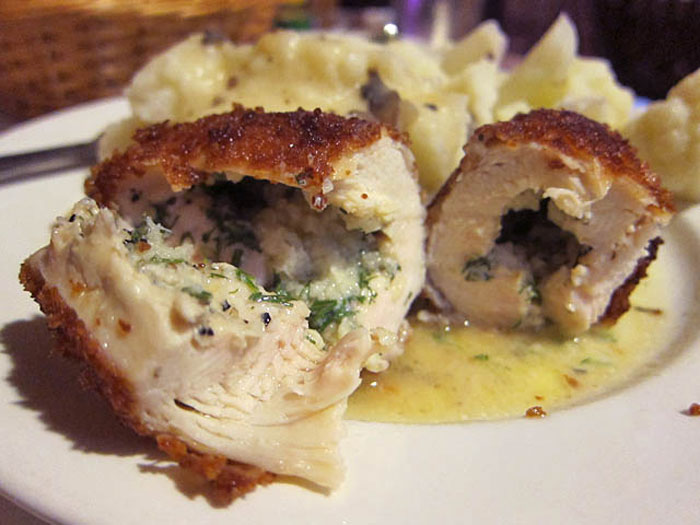 Old-school delicacy, sliced stuffed chicken roulade with herbs and mashed potatoes on a white plate.
