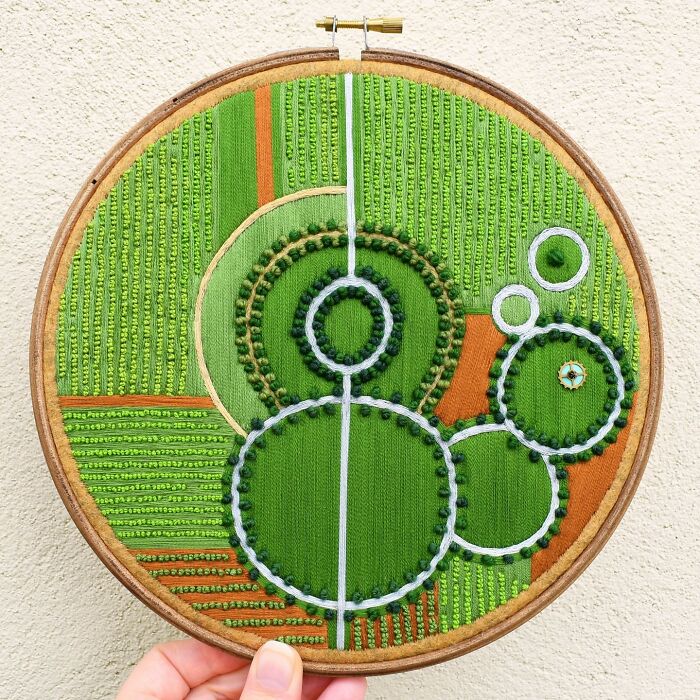 Landscape embroidery in a circular frame featuring abstract green fields and circles.