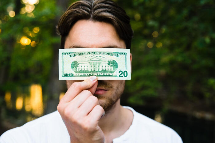 Man holding a $20 bill over eyes, outdoors, symbolizing lost connection with former best friend.