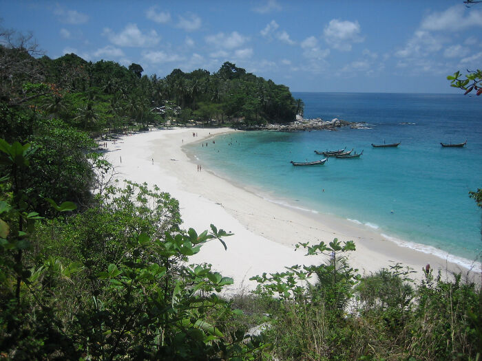 Pristine beach with turquoise water and white sand, surrounded by lush greenery and traditional boats.