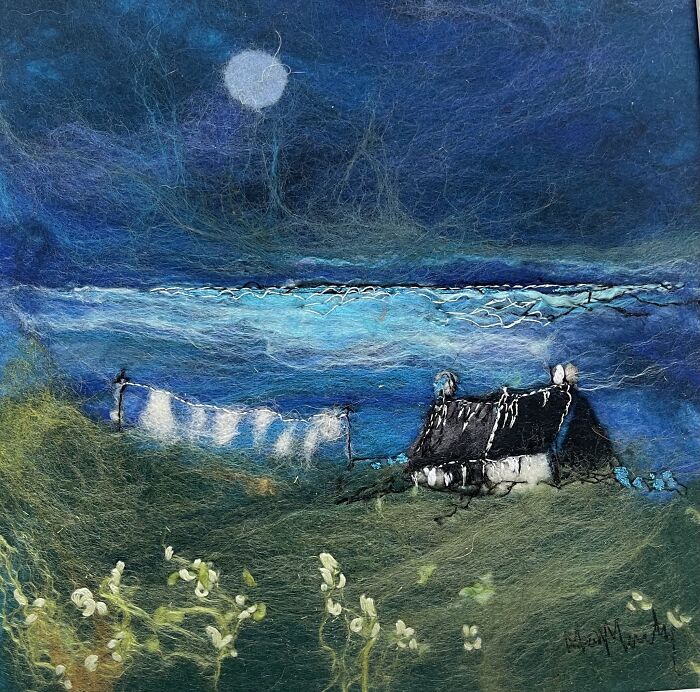 Fiber art by Moy Mackay depicting a serene night landscape with a cottage under a full moon.