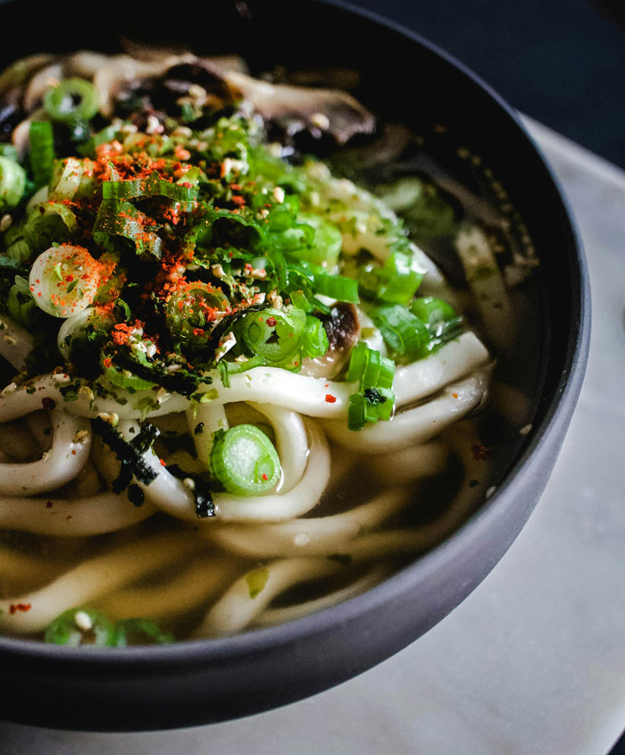 Close-up of a bowl of udon noodles topped with fresh green onions and spices, showcasing a delicious lazy meal option.