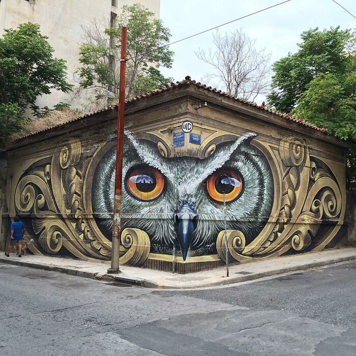 3D street art of an owl's face painted on a building corner, showcasing intricate details and vibrant colors.