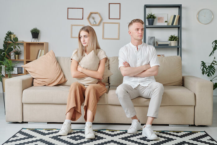 Couple sitting apart on a beige sofa, arms crossed, looking away, highlighting what type never date again scenario.