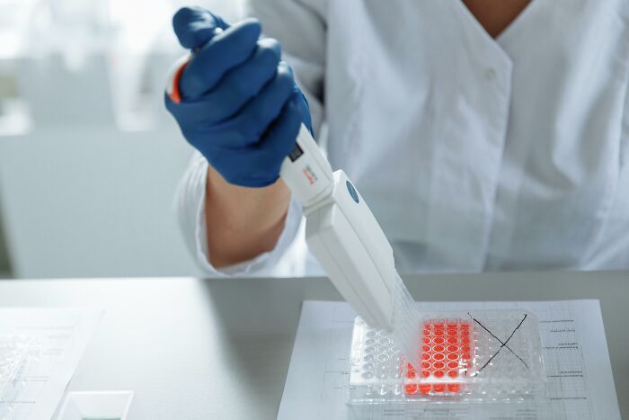 Person in a lab coat using a pipette with test samples, representing genetics research and data concerns.