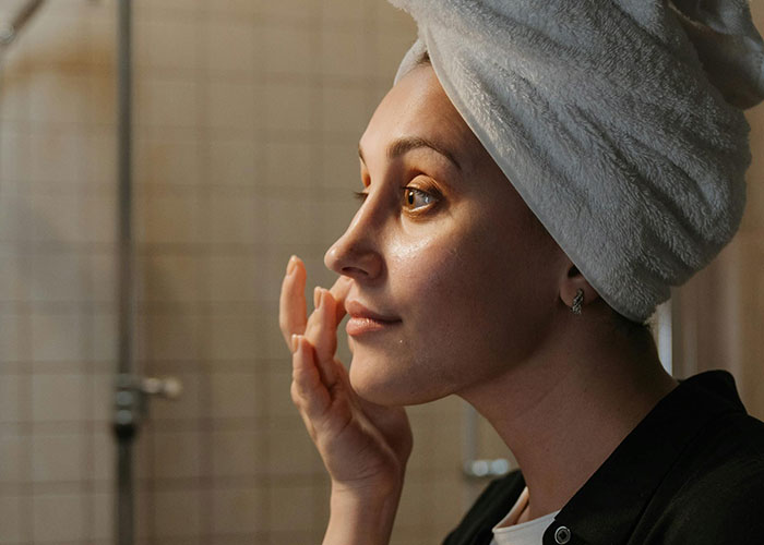 Woman applying skincare with towel wrap, exemplifying beauty tips.