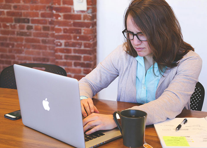 A woman in glasses works on a laptop at a desk, highlighting workplace elements and potential red flags.
