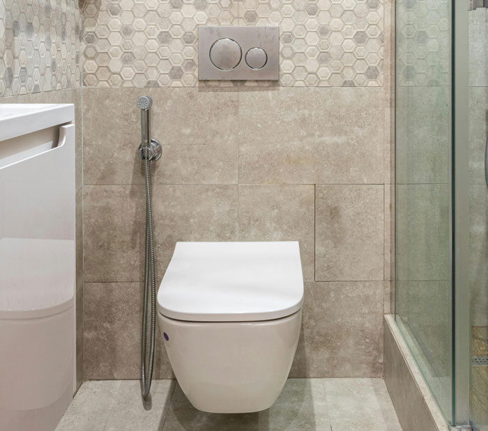 Modern bathroom with wall-mounted toilet and bidet spray, featuring beige tiles and geometric backsplash.