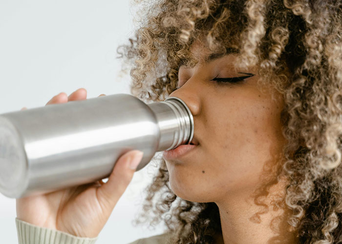 Woman drinking water from a metal bottle, highlighting beauty tips for hydration.