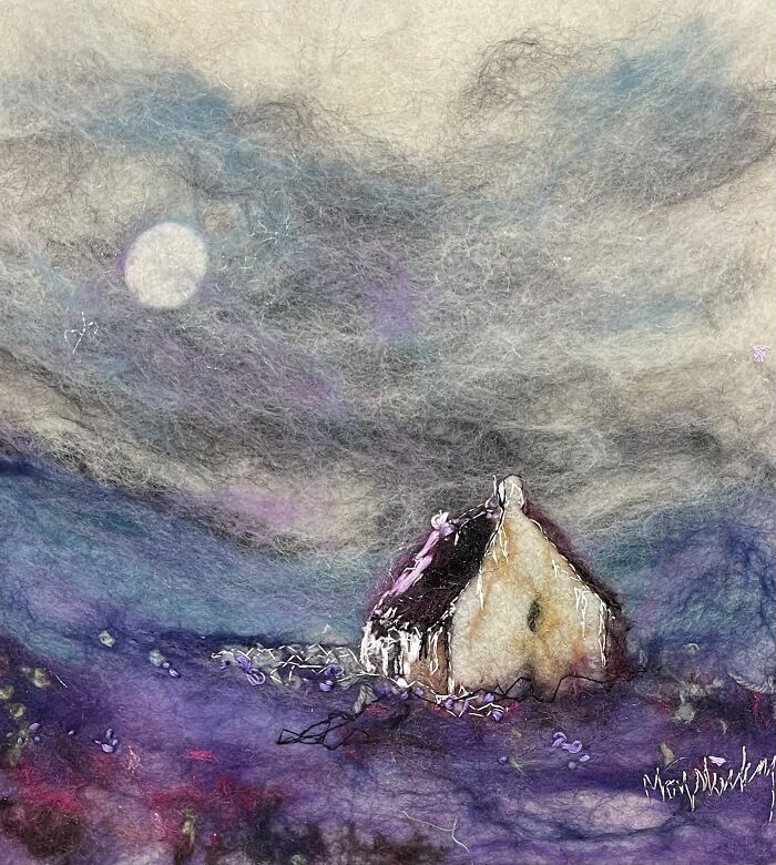 Fiber art depicting a serene landscape with a small house under a cloudy sky.