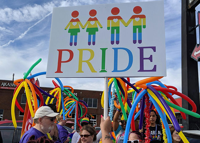 Pride parade with colorful balloons and a sign featuring rainbow figures holding hands.