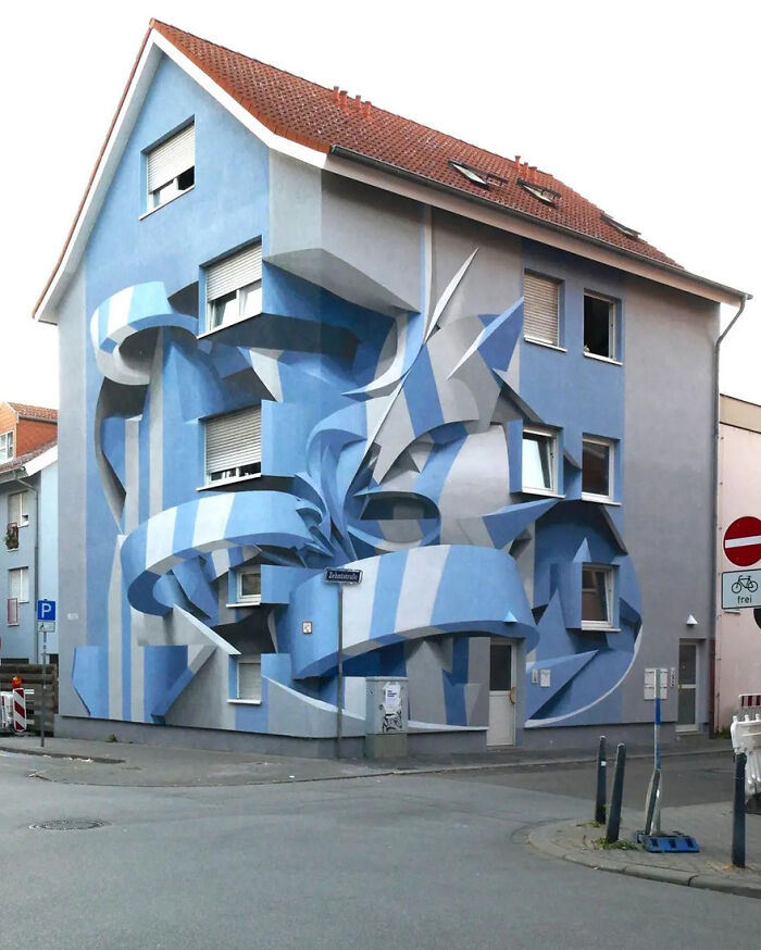 Mind-bending 3D street art on a house facade, featuring blue and white geometric patterns creating an optical illusion.