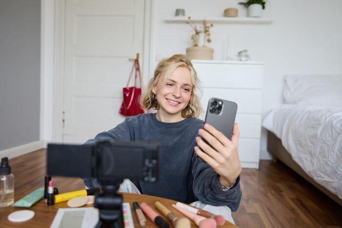 Young woman smiling, holding a phone for a video, surrounded by makeup products, reflecting on what type never date again.