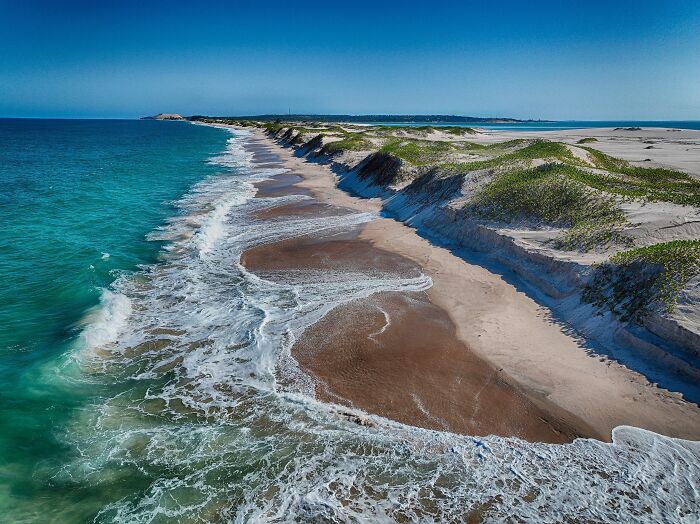 Expansive stunning beach with turquoise waves and sandy shores, enticing travelers to book a plane ticket.