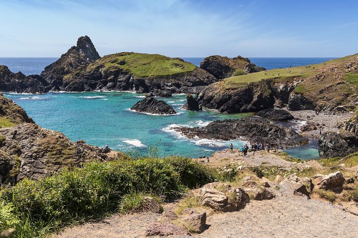 Stunning beach with turquoise waters, rocky cliffs, and lush greenery under a clear blue sky.