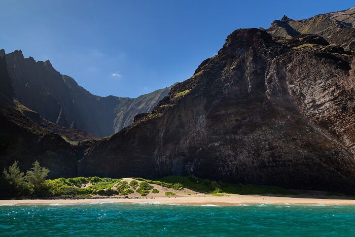 Stunning beach with clear blue water and rugged cliffs under a bright blue sky.