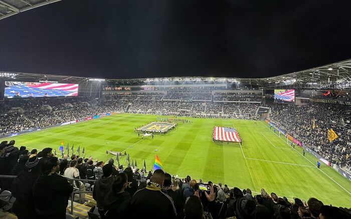 Packed soccer stadium at night with fans holding flags and teams lined up on the field in one of the cathedrals of soccer.