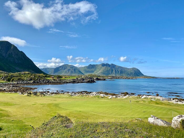Breathtaking golf course by a serene ocean with mountains in the background.