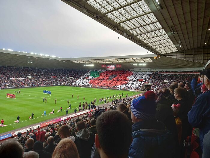 Crowded soccer stadium with fans displaying a large poppy mosaic, showcasing iconic cathedrals of soccer atmosphere.