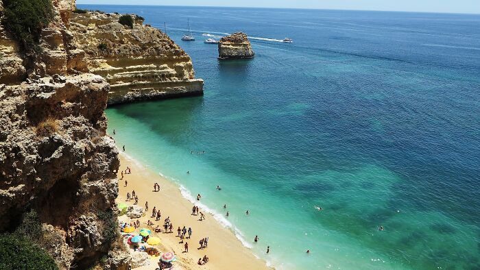 Stunning beach scene with turquoise waters, rocky cliffs, and sunbathers enjoying the scenic coastline.
