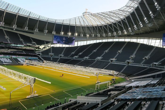 Modern cathedral of soccer with empty stands and sunlight lighting the green field inside a large stadium.