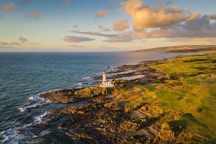 A breathtaking golf course beside rocky coastline and a lighthouse, highlighting global golfing destinations.