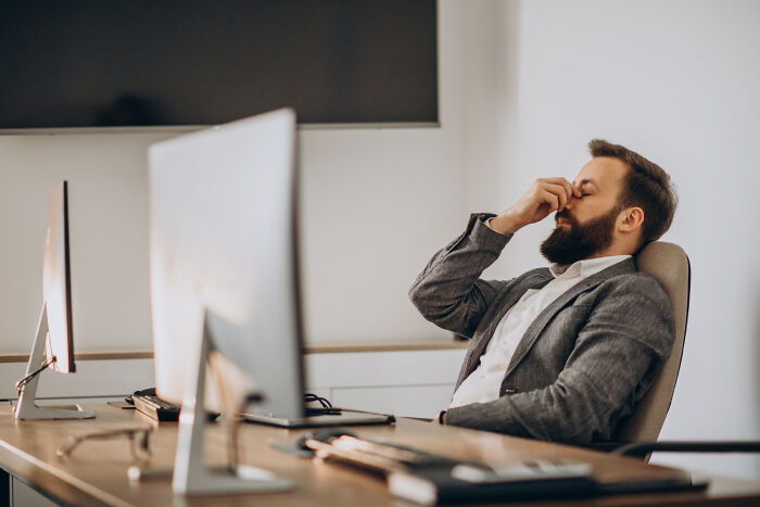 Man in a formal suit sitting at a desk, appearing frustrated at work, symbolizing petty revenge scenarios.