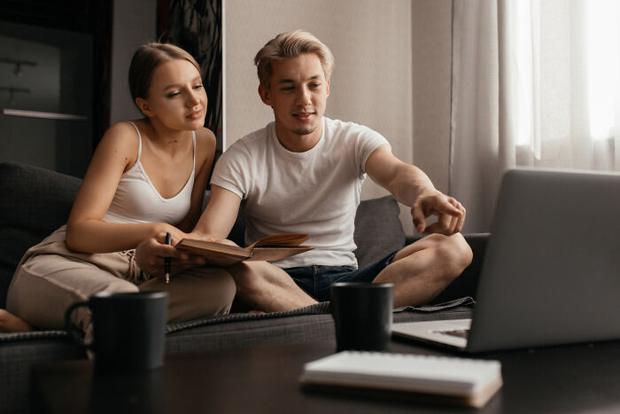 A couple in casual attire sharing a book and pointing at a laptop, showcasing green flags on a first date.