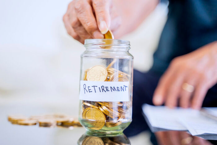 Hand placing coin in a jar labeled "Retirement," symbolizing saving habits.