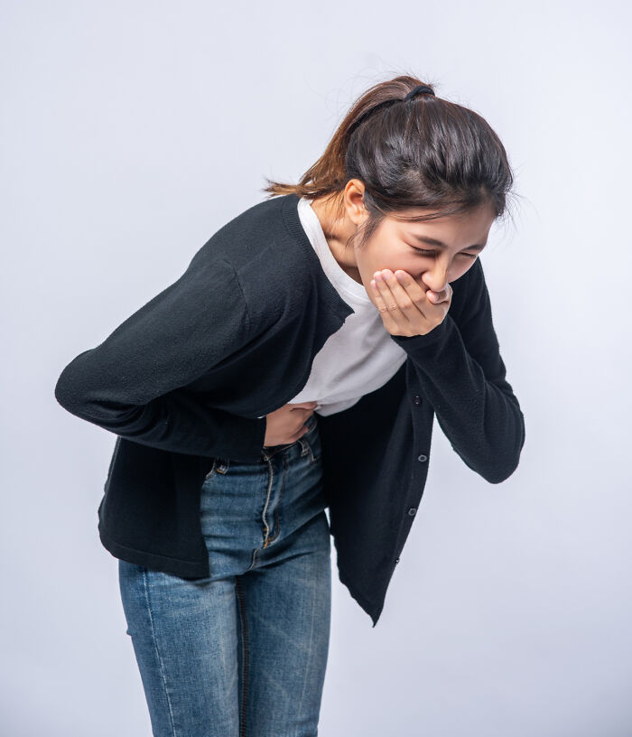 Woman in discomfort holding stomach, wearing casual jeans and black cardigan, possibly reacting to stressful job situation.
