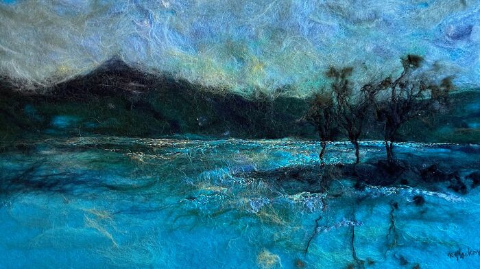 Fiber art landscape by Moy Mackay depicting trees and a mountain under a cloudy sky in vibrant blues and greens.