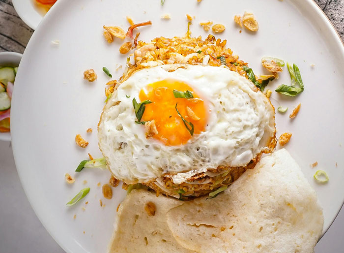 A lazy meal featuring fried rice topped with a sunny-side-up egg and garnished with herbs on a white plate.