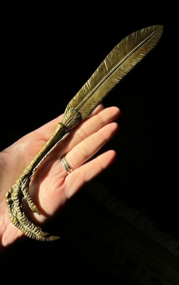 Hand holding a bizarre thrift find: a metal claw-shaped feather decor item.