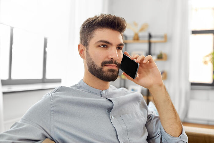 Man in casual shirt, sitting indoors, talking on phone, concept of work revenge.